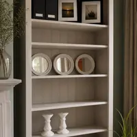 Close view of the upper shelves of the painted pine bookcase, showing the moulded cornice, tongue-and-groove back panel, black magazine files, two framed coastal photographs and three round white-framed mirrors