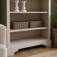 Lower shelves of the handmade bookcase holding two woven wicker storage baskets and a pair of ceramic candlesticks, showing the shaped bracket plinth above a light oak floor