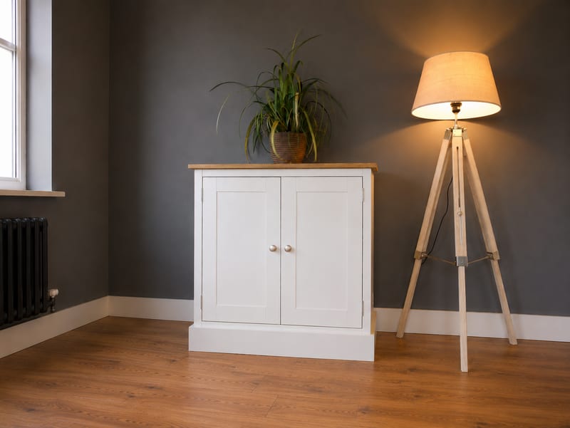 Compact white painted two door sideboard with a solid oak top, standing against a dark grey wall beside a wooden tripod floor lamp with a trailing plant on top