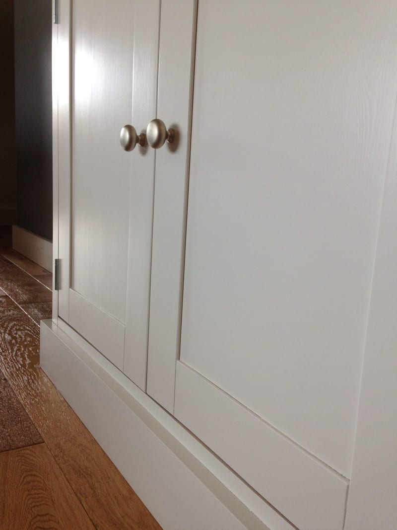 Angled close view along the front of the painted sideboard, showing its two Shaker doors, brushed nickel mushroom knobs and the moulded plinth running beneath