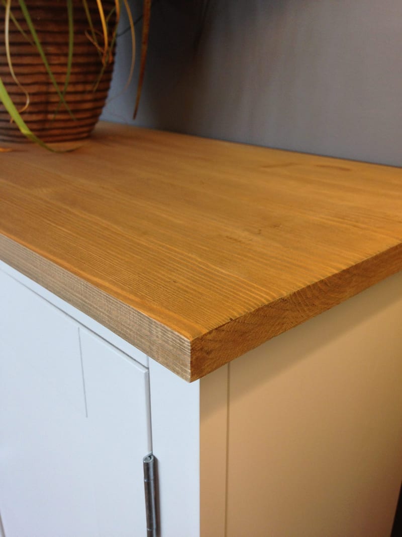 Close-up of the corner of the sideboard's solid oak worktop, showing the oiled grain, sawn edge profile and the slight overhang above the white painted carcass