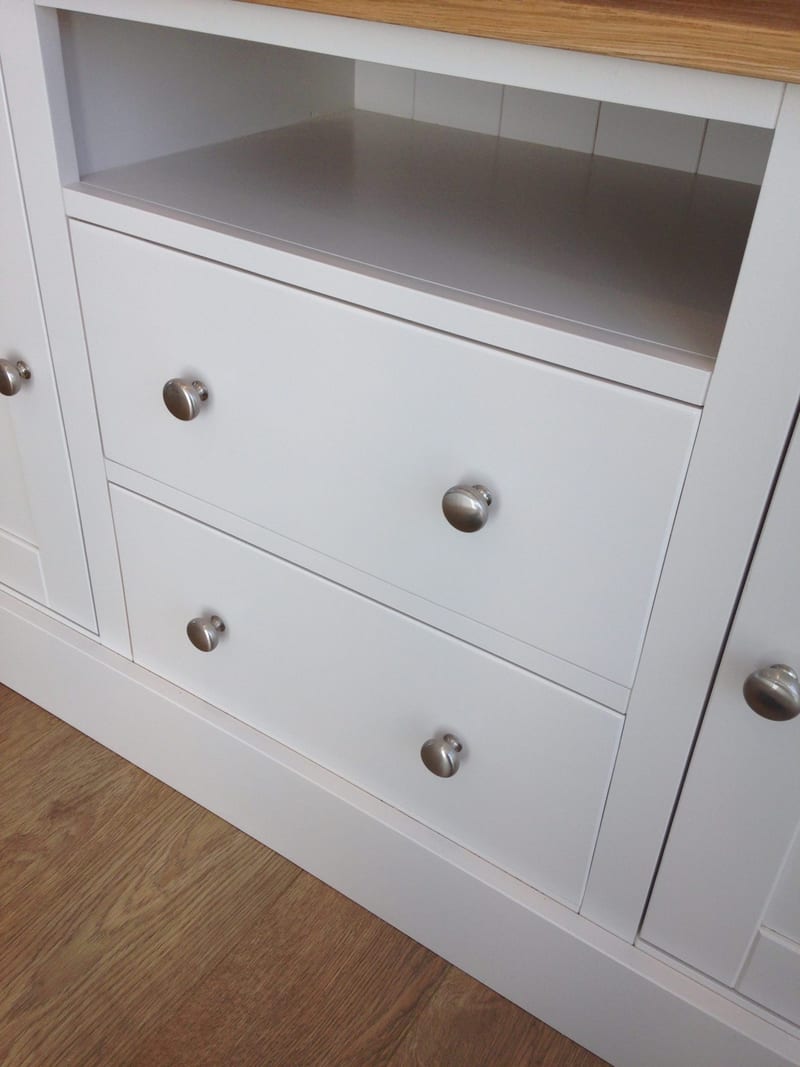 Close angled view of the TV unit's two central drawers with brushed nickel knobs, the open media shelf above them and the flanking cupboard doors, set on an oak floor