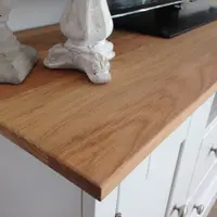 Close-up of the corner of the American blonde oak worktop, showing the oiled grain and sawn edge beside a pair of stone candlesticks and the base of the television
