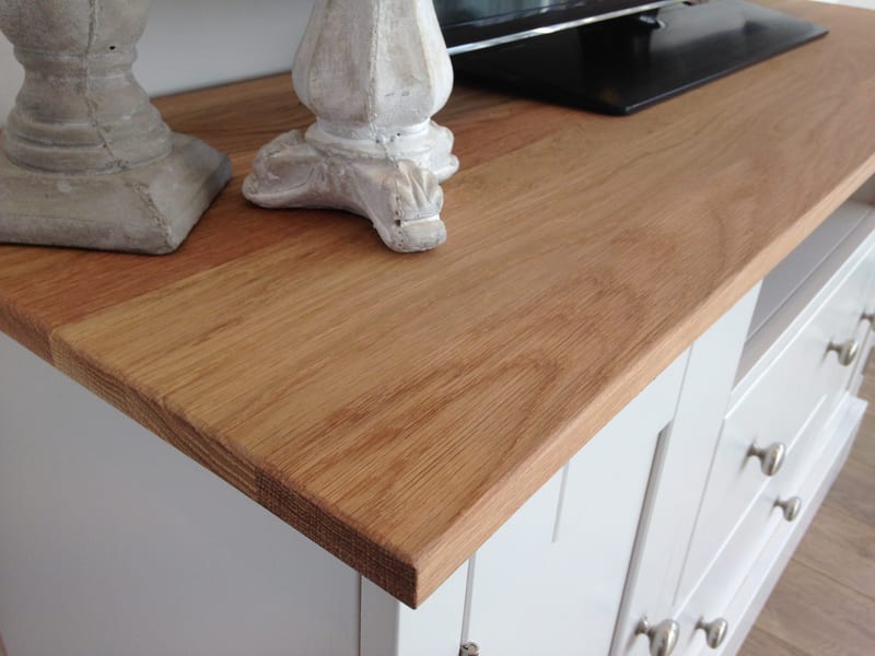 Close-up of the corner of the American blonde oak worktop, showing the oiled grain and sawn edge beside a pair of stone candlesticks and the base of the television