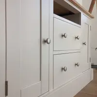 Low angled view along the front of the painted TV cabinet, showing the Shaker doors, central drawer stack, open media shelf and the overhang of the solid oak worktop