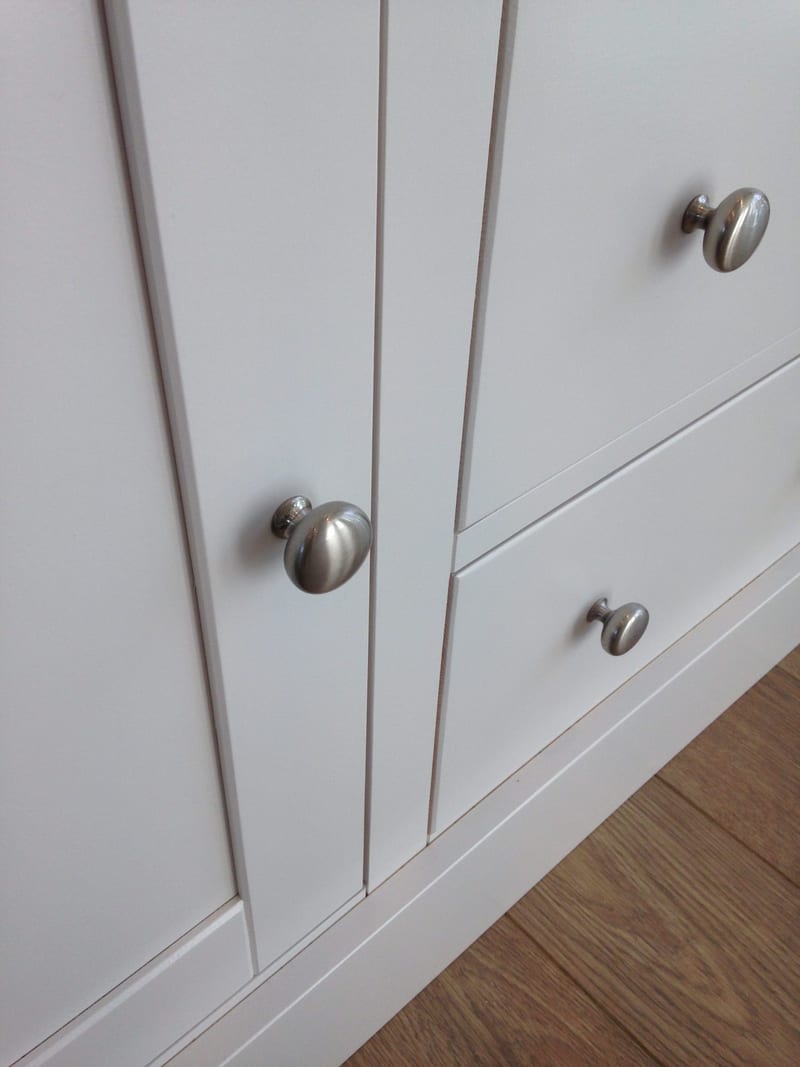 Close detail of the Shaker door frames and brushed nickel mushroom knobs on the painted TV unit, with the drawer front and plinth meeting an oak floor