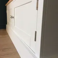 Low angled view along the front of the TV cabinet, showing the recessed Shaker door panels, a brushed nickel knob and the long brushed steel hinges