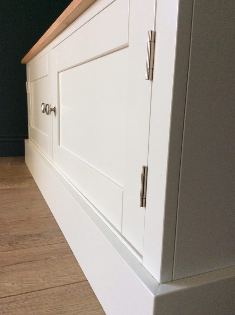 Low angled view along the front of the TV cabinet, showing the recessed Shaker door panels, a brushed nickel knob and the long brushed steel hinges