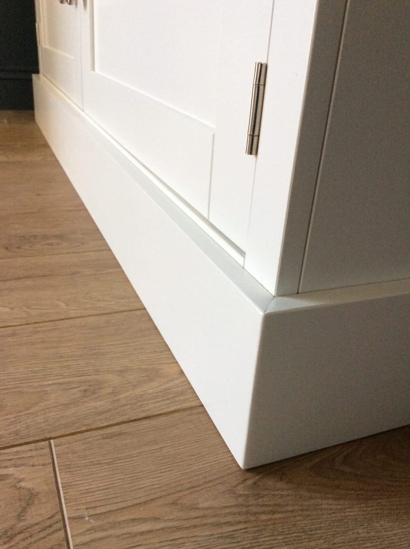 Close detail of the base of the TV stand where the Shaker door meets the stepped painted plinth above a light oak floor