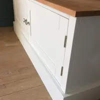 Angled corner view of the TV unit showing the solid oak worktop, one Shaker door with brushed nickel knob and hinges, and the painted plinth below