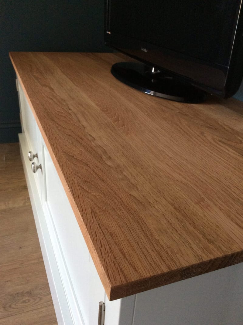 Close-up of the solid oak worktop surface showing its open grain and sawn edge, with the black pedestal base of a flatscreen television resting on it