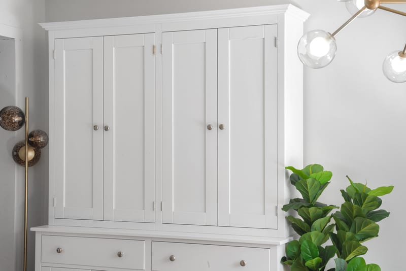The upper section of the Welsh dresser with its four tall panelled doors and moulded cornice, lit by a brass globe pendant beside a fiddle leaf fig