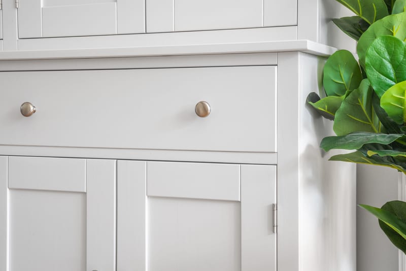 Close view of a base drawer front and cupboard doors of the painted dresser with brushed nickel knobs, framed by the leaves of a fiddle leaf fig
