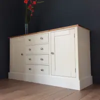 Angled view of the cream sideboard on oak laminate flooring, showing the honey pine top, four drawers with brushed nickel knobs between two shaker doors and the deep plinth base