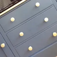 Overhead angled view across the navy drawer fronts, showing the round brass knobs, the crisp shadow gaps between the drawers and the lower edge of the television screen above