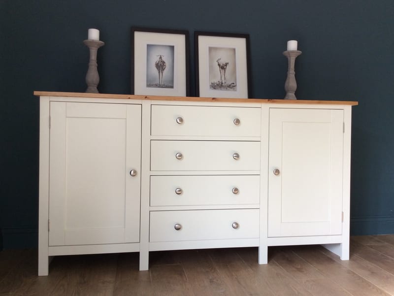 Slightly angled view of the cream sideboard styled with two framed black and white animal prints and a pair of grey wooden candlesticks holding white pillar candles on the pine top