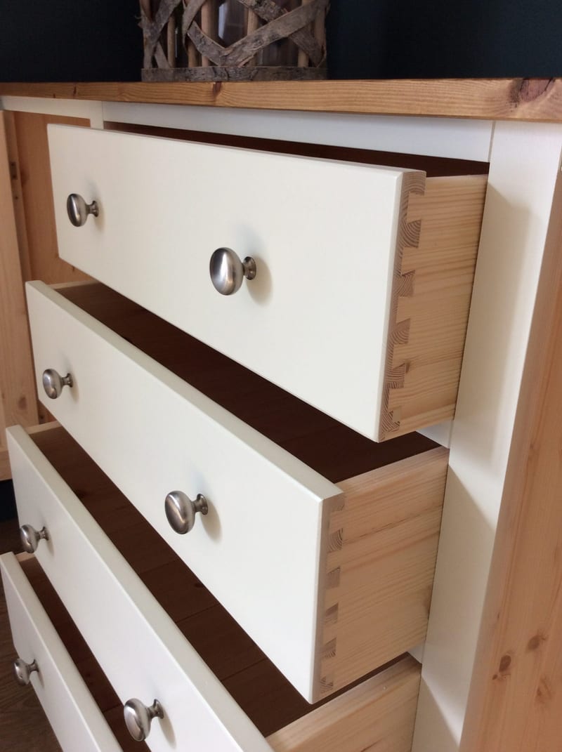 Close detail of the pulled out drawers, showing the hand-cut dovetail joints at the corners of the natural pine drawer boxes behind the cream painted fronts and their brushed nickel knobs
