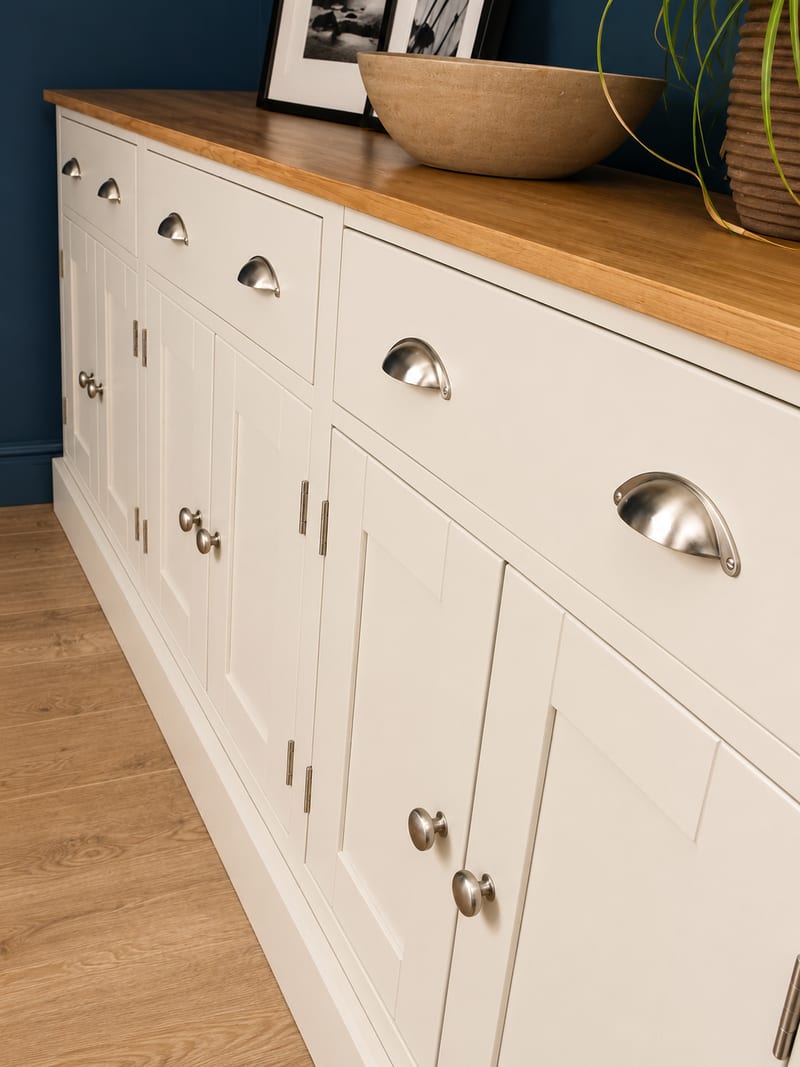 Close angled view of the sideboard front, showing the brushed nickel cup handles on the drawers, the round knobs on the shaker doors and the oak top with a stone bowl resting on it