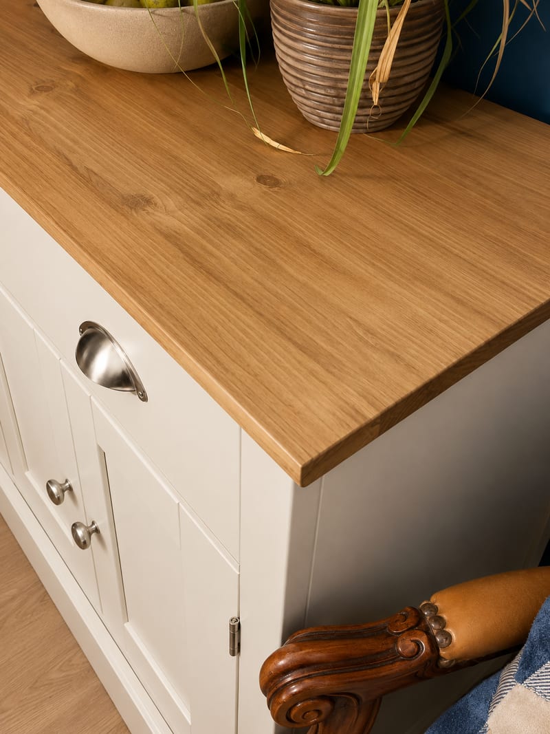 Detail of the right-hand corner of the oak top, showing the grain and thick square edge, a cup handle and two knobs on the cream painted side, and a leather armchair arm below