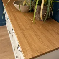 High view down onto the oak top of the cream painted sideboard, showing the grain and thick square edge beside a stone bowl and a ribbed plant pot, with cup handles below at the left