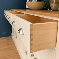 Angled view with all three drawers pulled open, showing the solid oak drawer boxes and hand-cut dovetail joints against the cream painted fronts and their brushed nickel cup handles