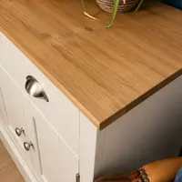 Detail of the right-hand corner of the oak top, showing the grain and thick square edge, a cup handle and two knobs on the cream painted side, and a leather armchair arm below
