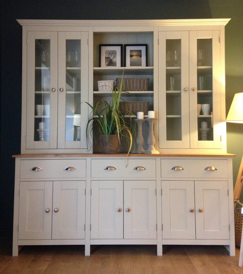 Full view of the cream painted Welsh dresser against a dark wall, with four glazed doors, open centre shelves holding framed prints and wicker baskets, and six cupboard doors below