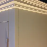Close detail of the painted cornice at the top corner of the dresser, showing the stepped moulding, the flat side panel and a brushed nickel hinge on the edge of the cupboard door