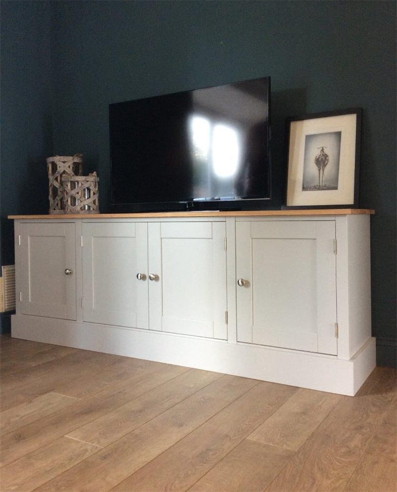 Pale grey 6ft TV media unit with full height cupboard doors across the front and a solid oak top, with a television, a framed print and woven lanterns on top against a dark teal wall