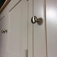 Close view of a round brushed nickel knob on a painted door, with two nickel hinges on the neighbouring door, a further pair of knobs beyond and the corner of the oak top at the upper left
