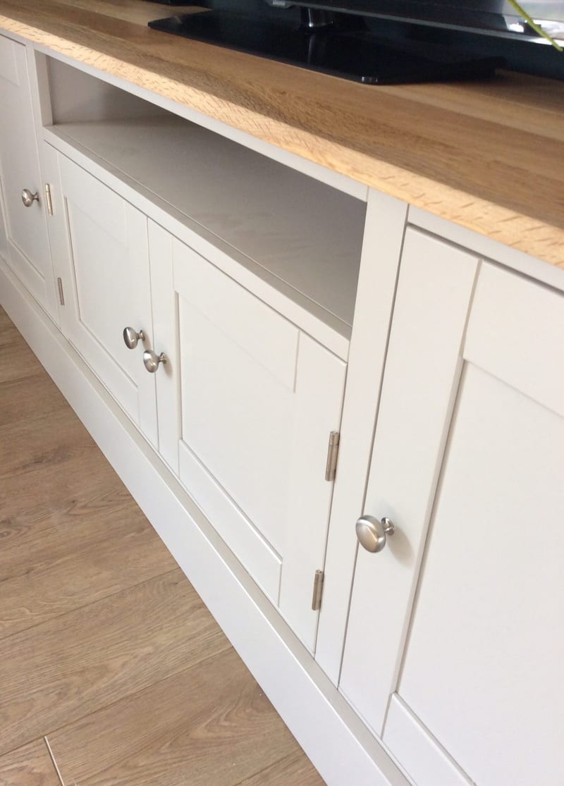 Close view of the open shelf recess in the painted media unit, showing the painted shelf inside, the sawn edge of the oak top above and the flanking doors with brushed nickel knobs