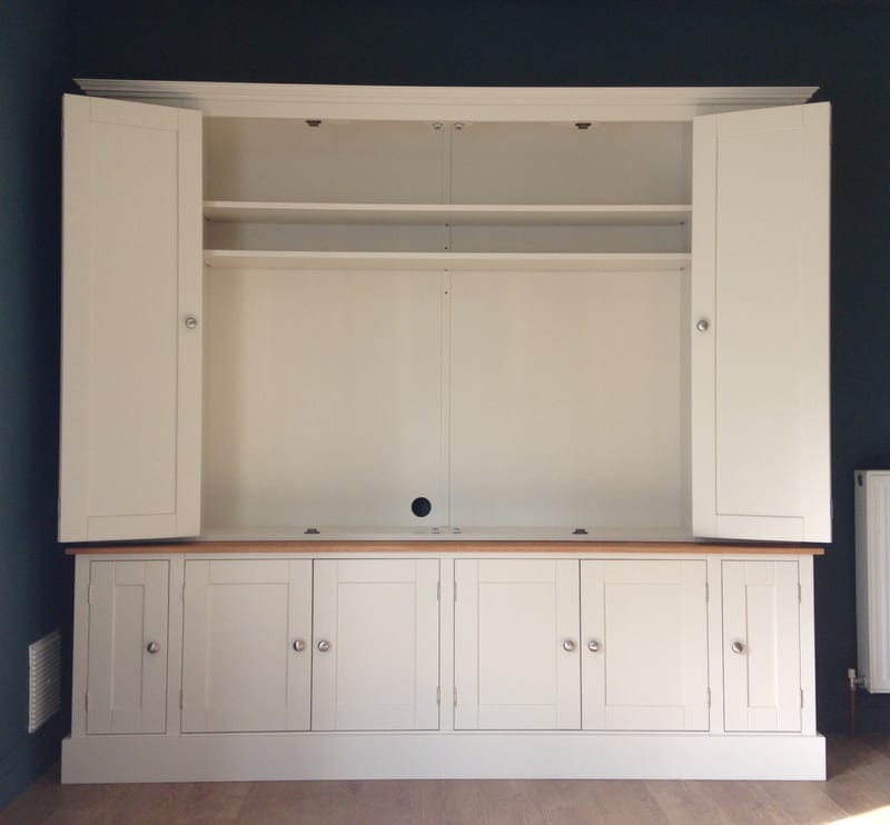Front view with both pairs of bifolding doors opened right back, showing the empty painted interior, two full-width shelves and the cable hole in the back panel above the oak worktop