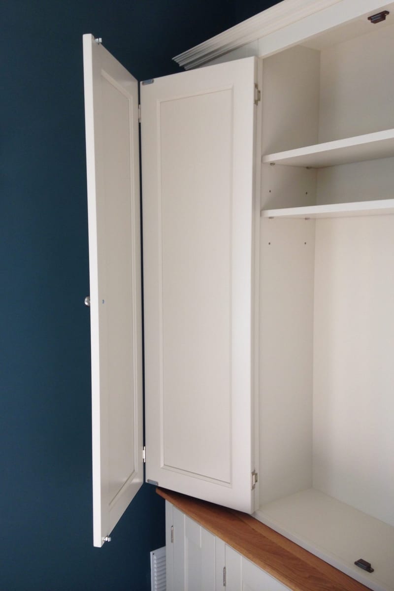Close view of one pair of bifolding doors folded back beside the dark blue wall, showing the shaker panel faces, brushed nickel knob and the painted interior shelves behind