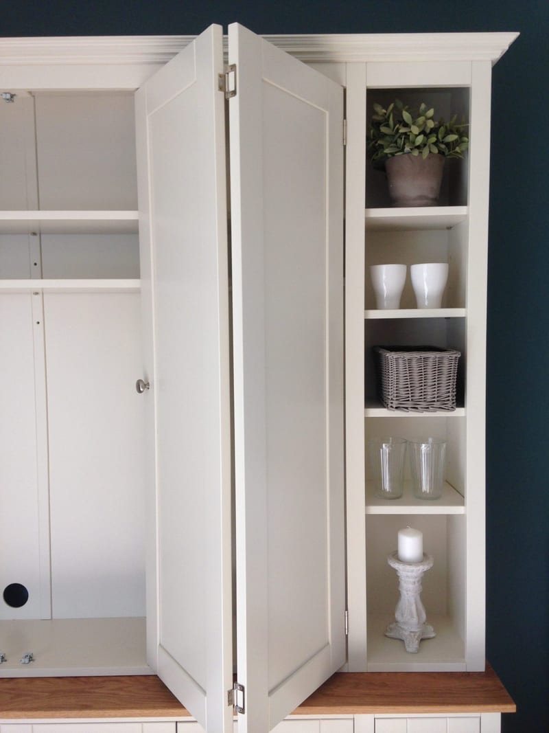 Close view with one pair of bifolding doors folded open, showing the empty shelved interior on the left and the end shelves holding a potted plant, white cups, a wicker basket and glass tumblers