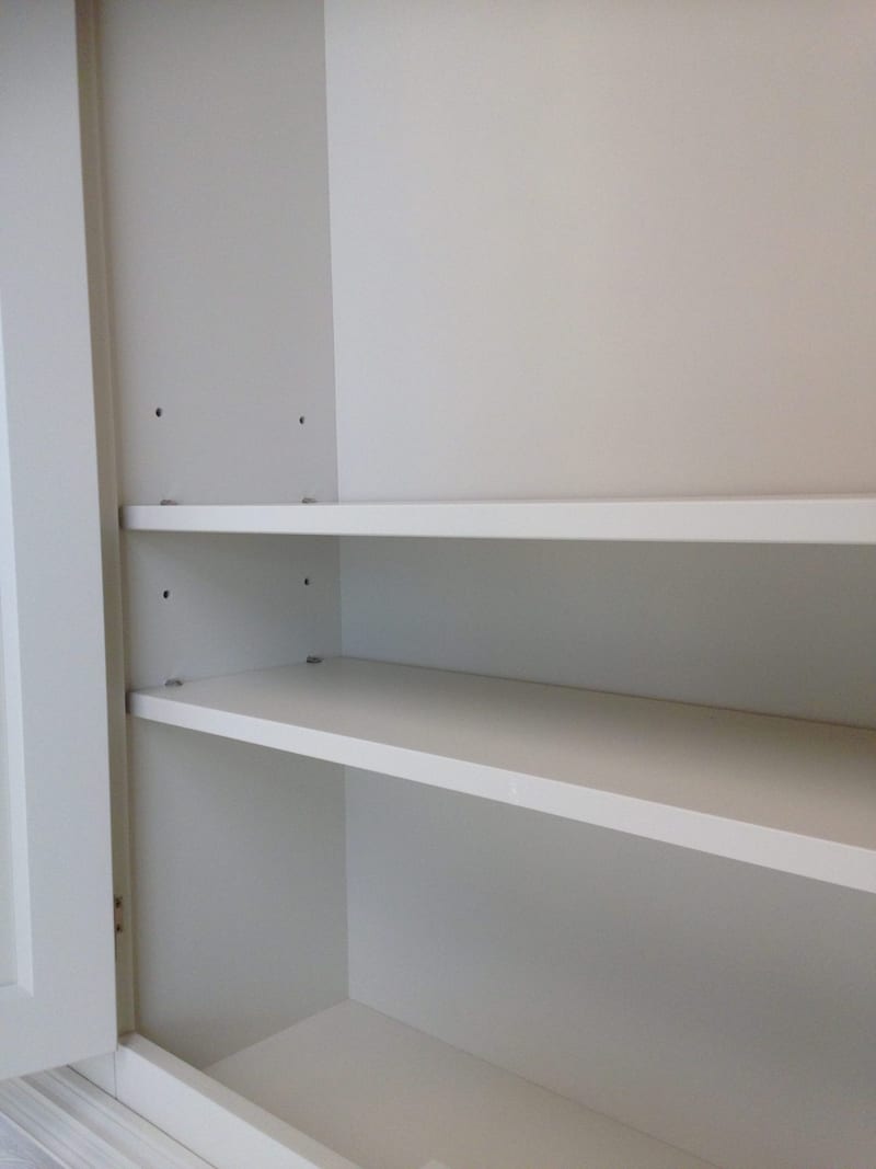 Close view inside one of the upper cupboards, showing two painted shelves, the rows of adjustment holes in the side panel and the smooth painted back boards