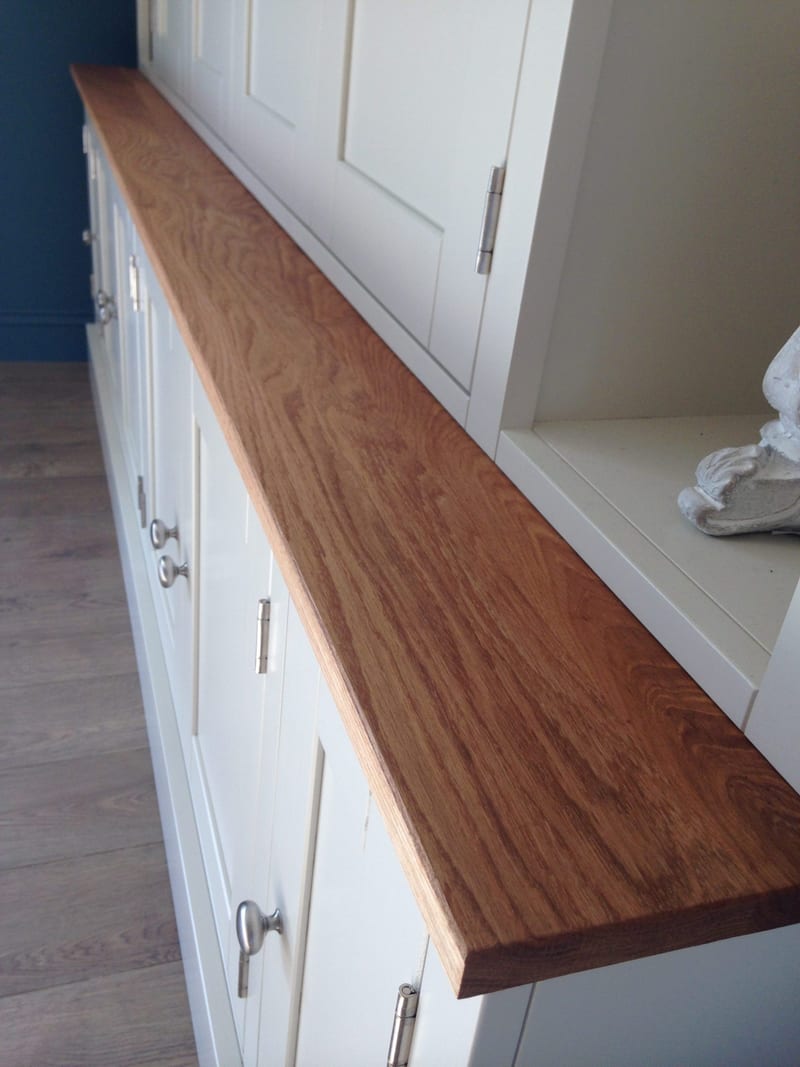 Angled detail of the oiled oak worktop running the length of the base, showing the grain and sawn edge above the painted doors, brushed nickel knobs and steel hinges