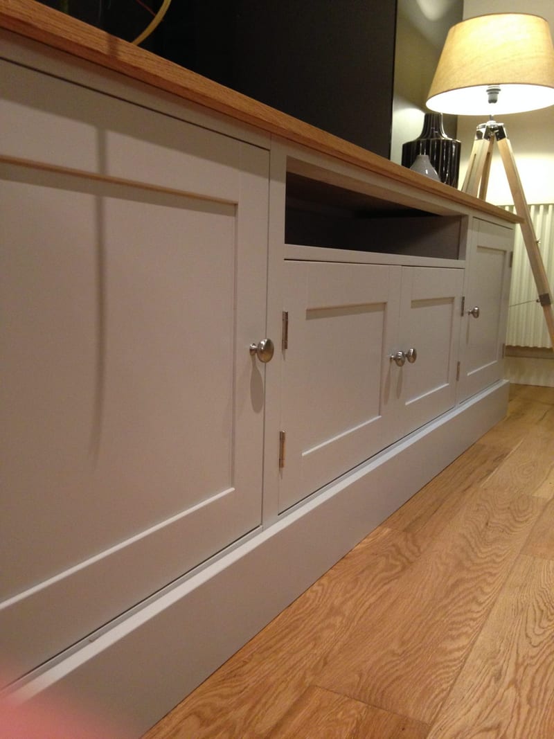 Low angled view along the front of the media unit, showing the end cupboard, the open media shelf, brushed nickel knobs with teardrop backplates and a tripod lamp beside the oak floor