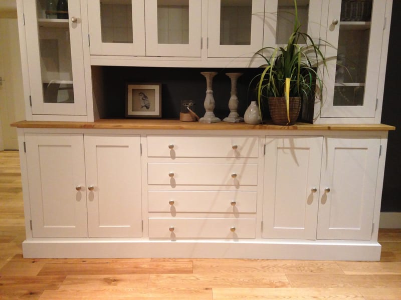 Front view of the base and open display shelf, showing four cupboard doors, four central drawers with pairs of brushed nickel knobs and a framed print, candlesticks and a plant on the pine top
