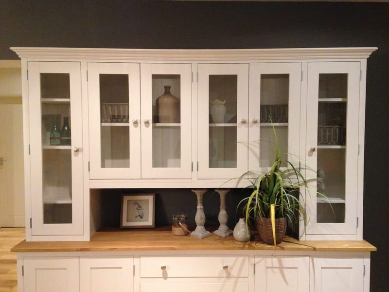 Front view of the glazed upper section, six glazed doors revealing wicker baskets, green glass bottles and a stoneware flagon above the open shelf holding candlesticks and a spider plant