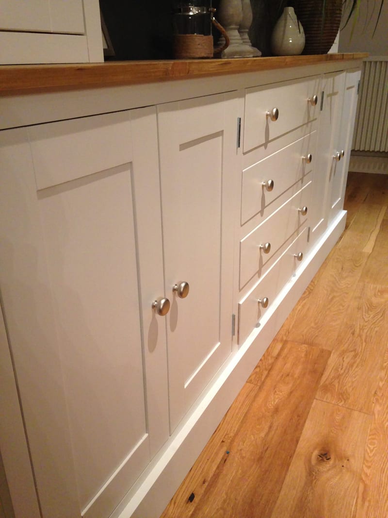 Low angled view along the base from the left, showing two shaker cupboard doors, four drawers on pairs of brushed nickel knobs, the pine top edge and the plinth on oak boards