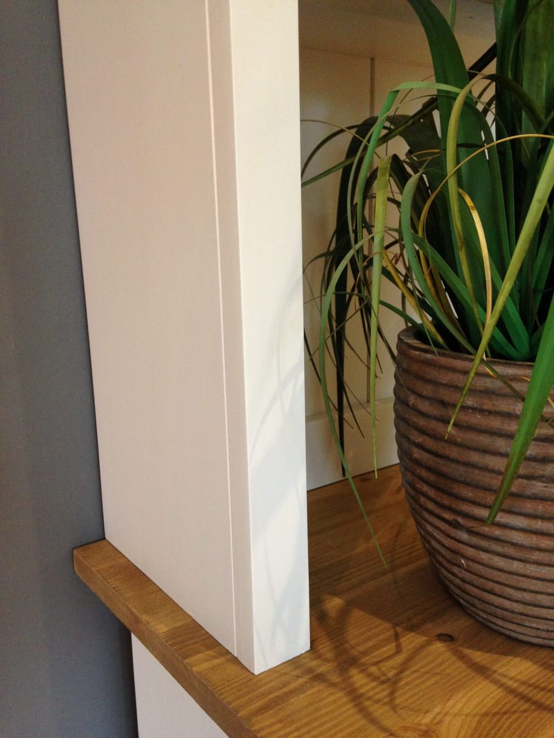 Detail of the painted side panel of the dresser top where it meets the waxed solid wood worktop, with a ribbed stone-effect pot holding a spiky green plant to the right