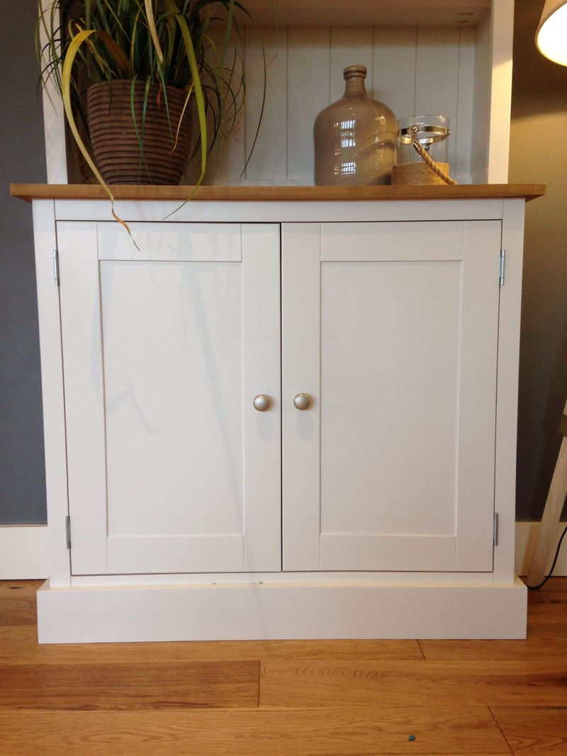 Front view of the painted base cupboard with two panelled doors, two round satin knobs and a waxed timber top, dressed with a potted plant, ceramic flagon and rope-handled lantern
