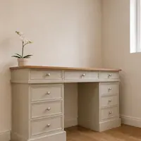 Angled view of the twin pedestal desk in a corner, showing the oak top, three frieze drawers, six pedestal drawers with satin nickel knobs and a white orchid standing on the left end