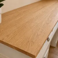 Close-up along the oak top, showing the open grain, medullary flecks and softly rounded edge, with a plant pot at the far end and two satin nickel drawer knobs below