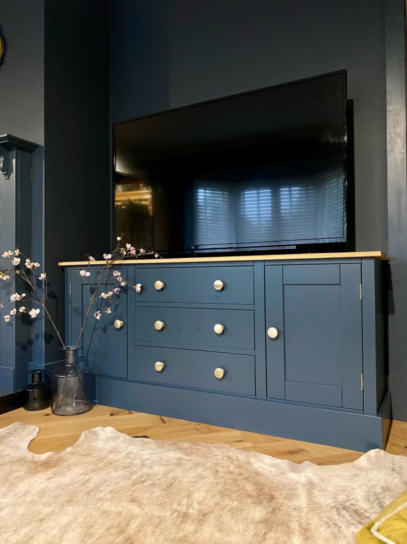 Navy blue painted 5ft TV media base unit with a solid oak top, three drawers between two cupboards with pale knobs, and a large television standing on top