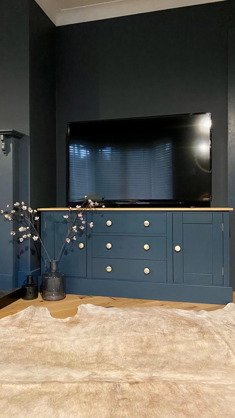 The navy unit set in a dark charcoal alcove with a large television on top, a cowhide rug across the herringbone oak floor and a painted newel post visible at the left of the room