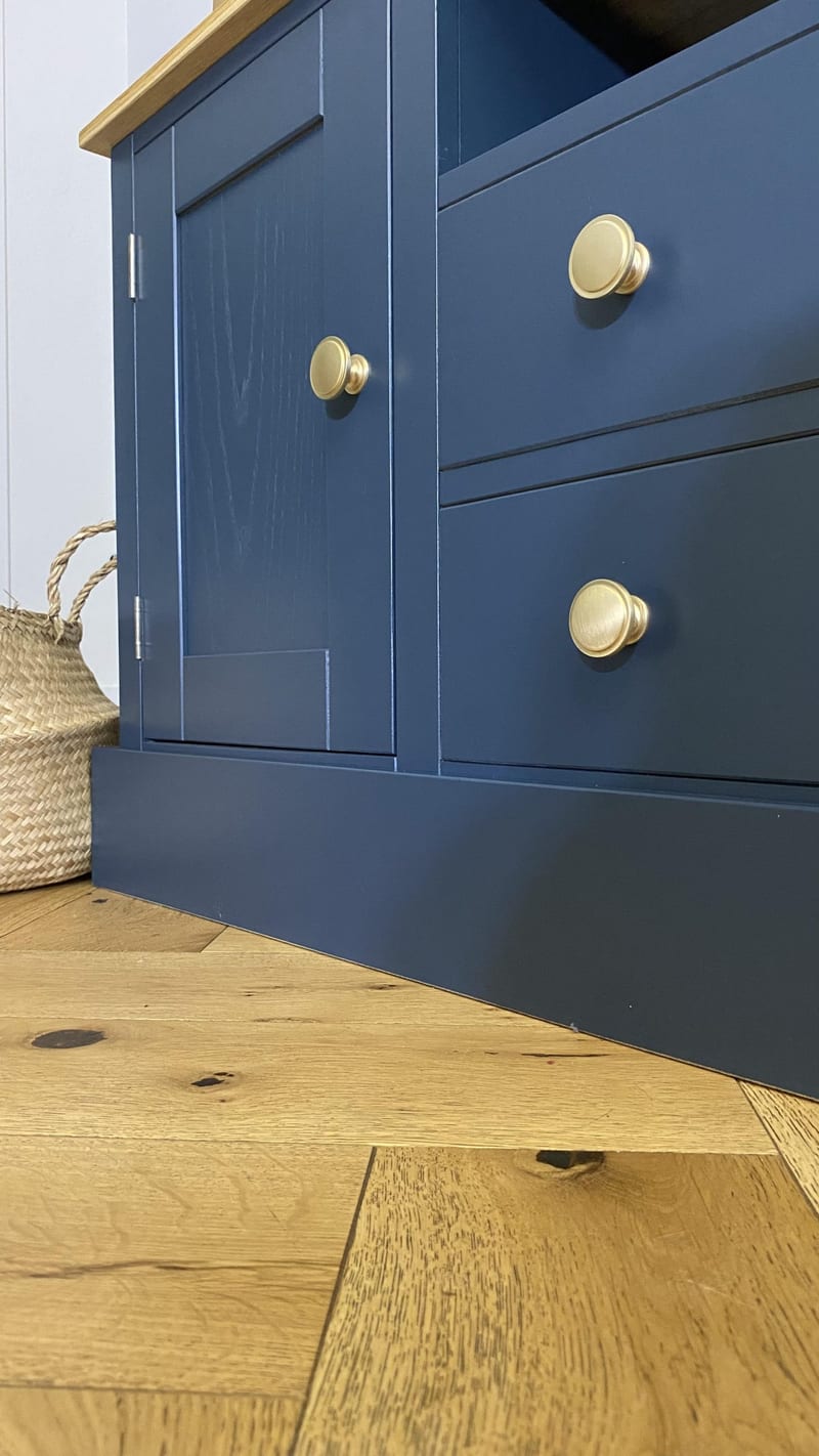 Detail of the navy painted door panel and drawer fronts, where the brushstrokes and timber grain show through the paint, above the plinth on a herringbone oak floor
