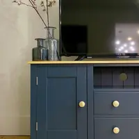 View of the left end of the unit, showing the panelled door, its brass knob and two chrome hinges, with a tall smoked glass vase of blossom, a smaller plain vase and the television on the oak top