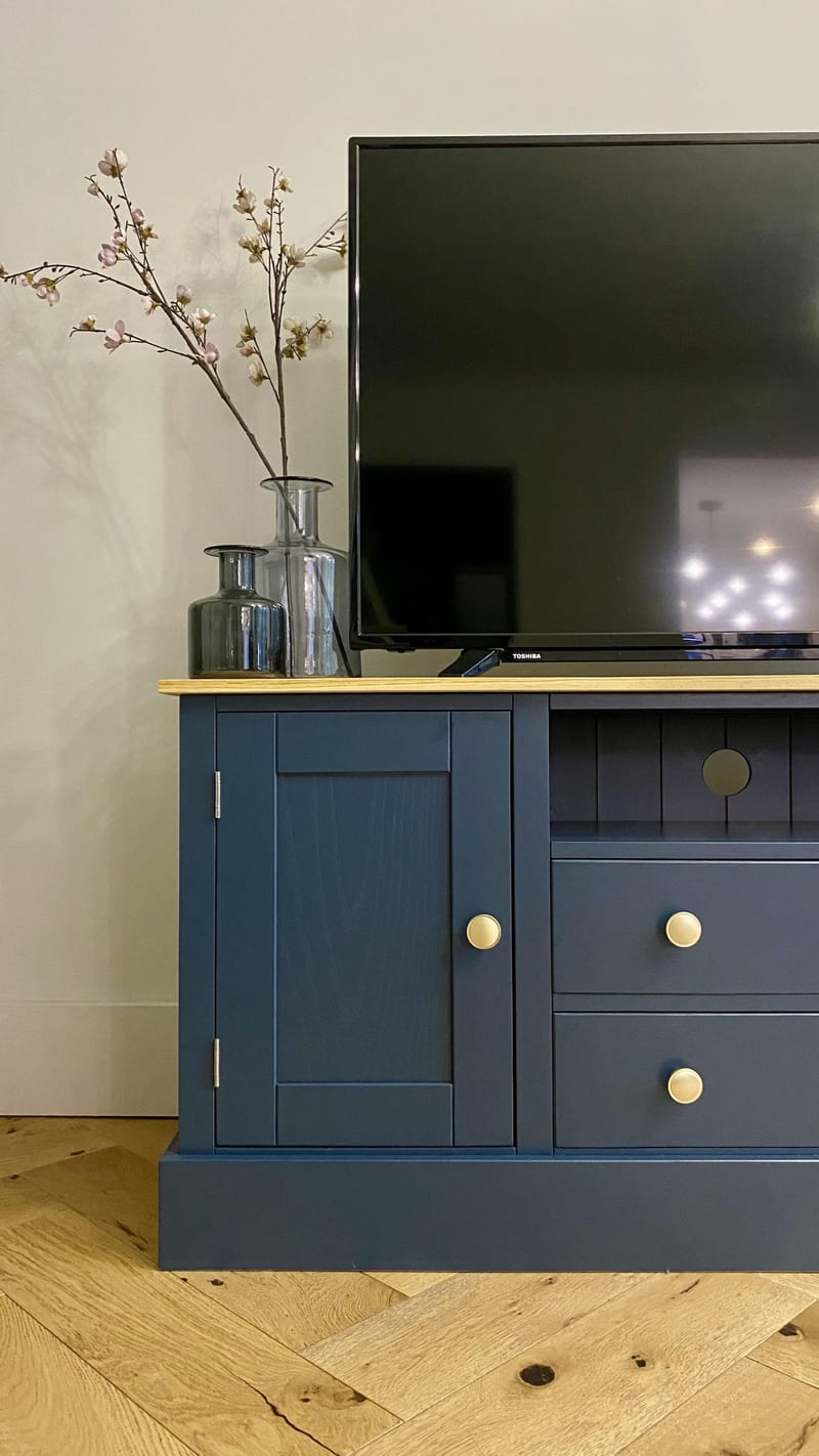 View of the left end of the unit, showing the panelled door, its brass knob and two chrome hinges, with a tall smoked glass vase of blossom, a smaller plain vase and the television on the oak top