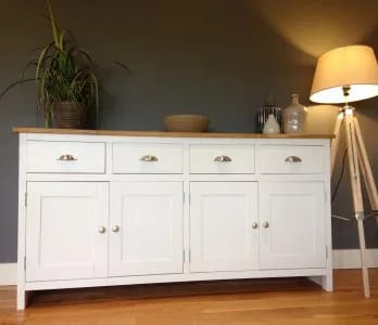 White painted 6ft sideboard with a solid oak top and four cup handled drawers over four shaker doors, against a grey wall beside a tripod floor lamp, with a plant and a wooden bowl on top